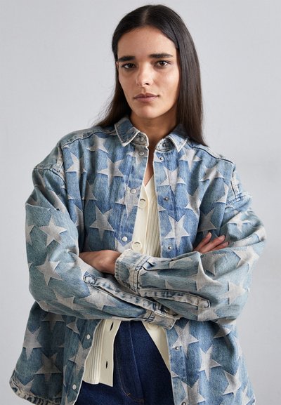 Denim jakna v svetlo modri barvi s velikimi belimi zvezdnimi vzorci, zapiranje na pritrdilne gumbe ter sproščenem kroju z dolgimi rokavi.