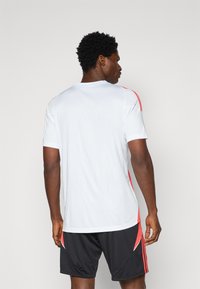 White athletic t-shirt with short sleeves, featuring red stripes along the shoulders. The design is simple and made from a lightweight material.