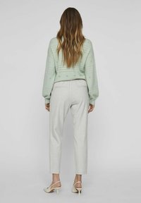 Pull en tricot vert clair avec motif perforé, associé à un pantalon gris clair ajusté et des escarpins à talons ouverts beige.