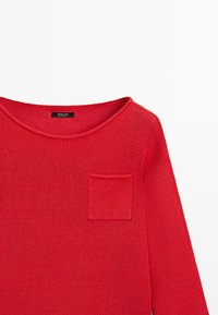 Maglione rosso lavorato a maglia con scollo tondo e una piccola tasca sul petto a sinistra.