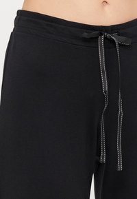 Svarta sweatpants med en mjuk textur, med elastisk midja, dragsko knuten med ett dekorativt band och kontrastsömnadsdetaljer.