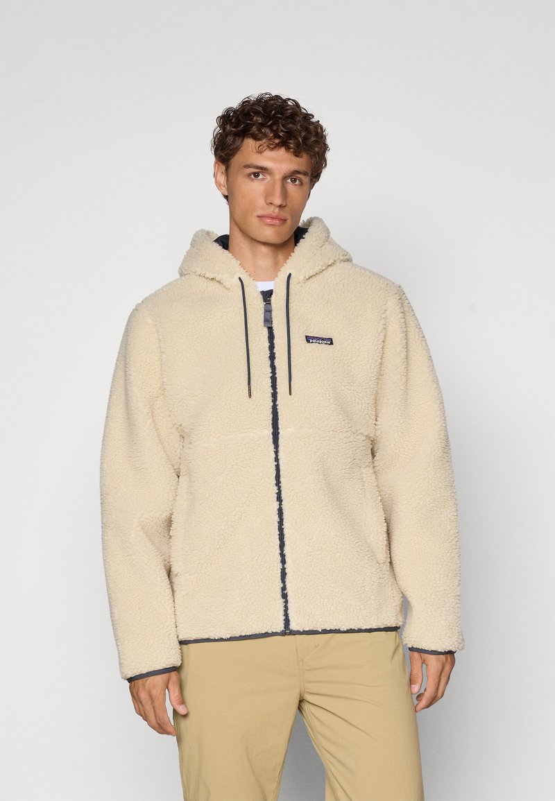 Haut à capuche en polaire couleur crème avec fermeture éclair sur le devant, cordons de serrage et accents bleu marine. Présente une coupe décontractée et un matériau doux et texturé.