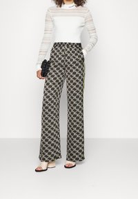 Pantalon large à motifs noirs et crème avec un design en chevrons, doté d'une taille à cordon et de poches latérales. Associé à un haut blanc ajusté.
