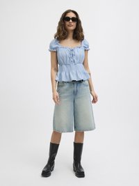 Light blue, short-sleeve top with a peplum hem, paired with knee-length denim shorts and black, flat-soled ankle boots.