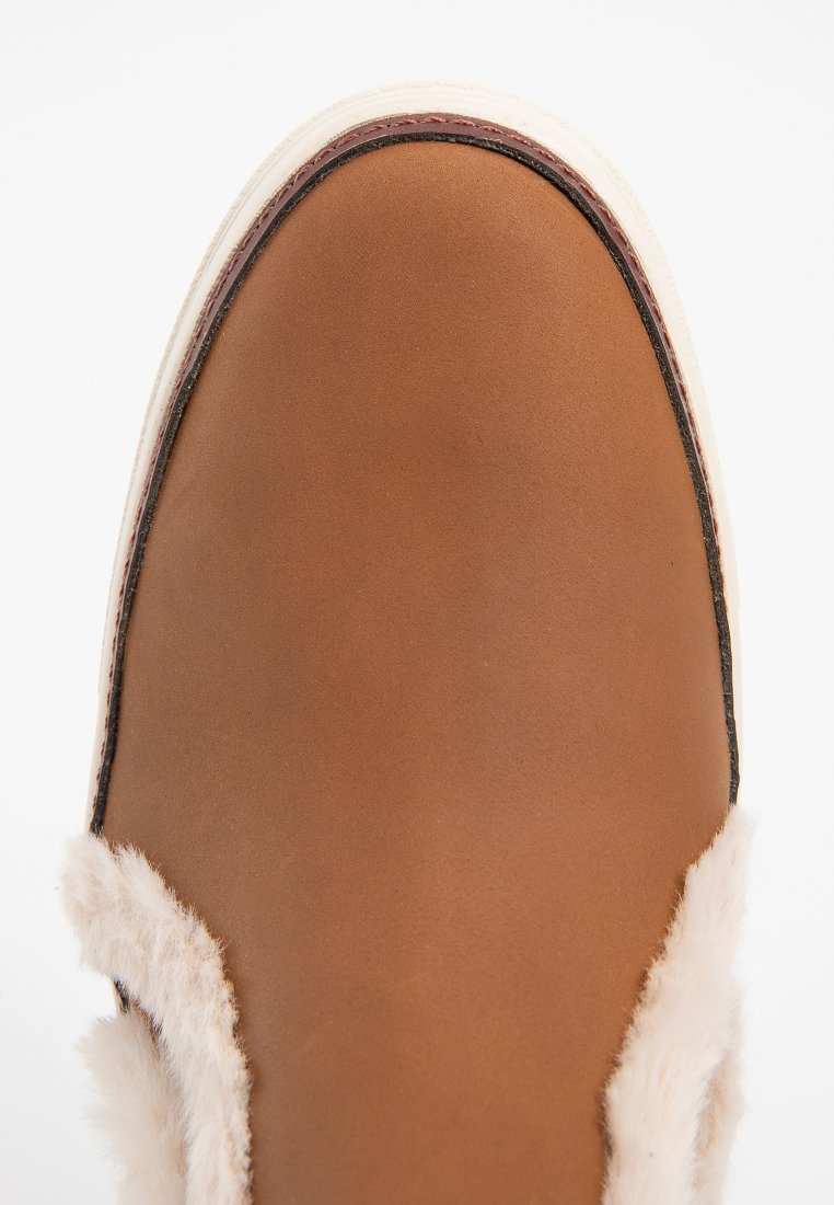 Chaussure en cuir marron avec une doublure crémeuse duveteuse, de forme arrondie et une fine semelle crémeuse. Présente des coutures visibles le long des bords.