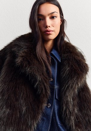 Neppels met een donkerbruine kleur over een spijkerjacket. De kraag heeft een zachte, pluizige textuur; knoopsluiting aan de voorkant met zichtbare stiksels.