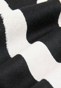 Tissu rayé noir et blanc, avec des rayures larges alternées. Le matériau semble texturé, montrant des détails tissés et des bords.