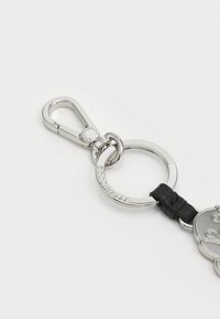 Metal keychain featuring a silver-tone finish, round ring, black leather strap, and an engraved brand logo. Includes snap hook closure.