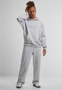 Hellgrau Hoodie mit einer Fronttasche und Kordelzug, kombiniert mit passenden grauen Sweatpants mit Seitennähten, getragen mit weißen Turnschuhen.