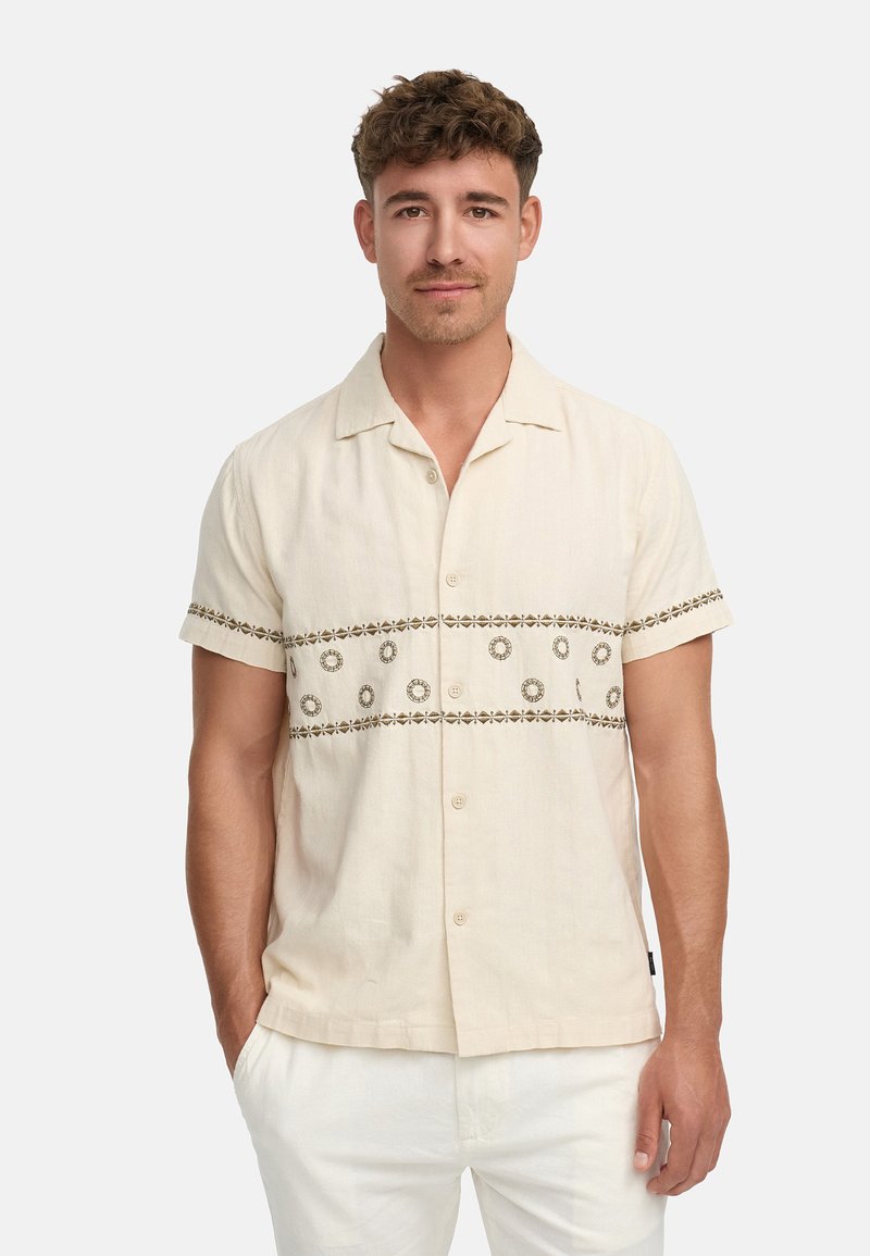Chemise à manches courtes beige à boutons, avec des broderies circulaires marron sur la poitrine et les poignets, fabriquée dans un tissu léger.