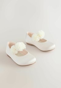 Valkoiset nahka-balletit, joissa on pyöristetty kärki ja iso valkoinen kukka-accentti hihnassa. Tasainen pinta ja matala korko.