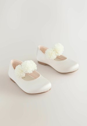Bílé kožené baletky s kulatou špičkou a velkým bílým květinovým akcentem na pásku. Hladký povrch s nízkým podpatkem.