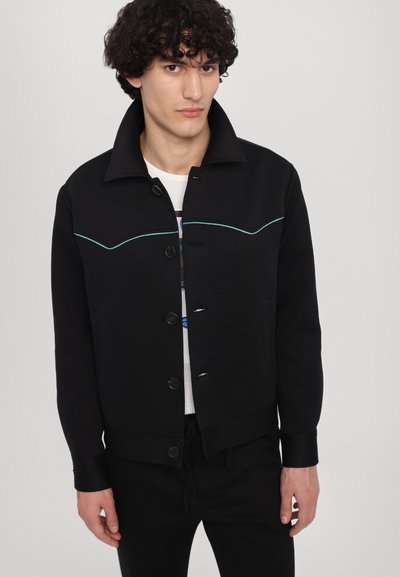 Black jacket with a structured collar, featuring turquoise stitching across the chest, button closures, and side pockets. Smooth fabric.