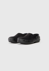 Par crnih klompi za klizanje Crocs s teksturiranim potplatima i podesivim remenima za petu na bijeloj pozadini.