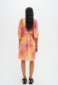 Abito a maniche corte, lunghezza ginocchio, in un motivo acquerello di tonalità rosa, arancione e giallo. Presenta una vita arricciata e maniche a palloncino.