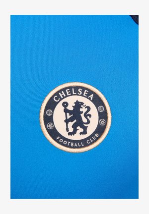 Blauw fabric met een gladde textuur bevat een cirkelvormig Chelsea Football Club-logo in het wit en zwart met een leeuwontwerp en decoratieve elementen.
