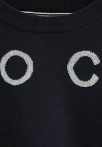 Marinblå tröja med stora vita broderade bokstäver "O" och "C" på framsidan. Texturerad stickad tyg med ribbat halslinning.
