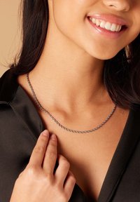 Draaiende zilveren ketting die op het sleutelbeen ligt, met een gladde metalen textuur en een subtiele glans tegen een donker blouse.
