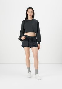 Svart cropped genser med lange ermer. Kombinert med en svart denim miniskjørt med frontlommer. Brukt med grå sokker og hvite joggesko.