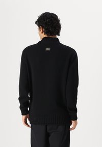 Μαύρος πλεκτός σκούφος με ψηλό ριμπ κολάρο. Διαθέτει μια διακριτική ετικέτα με λογότυπο στην πλάτη και ριμπ μανίκια και στρίφωμα. Κλασικός σχεδιασμός.