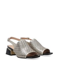 Metallisch silberne Slingback-Schuhe mit offenen Zehen, geometrischem Perforationsmuster, schwarzem quadratischen Absatz und Knöchelriemen. Glatte Textur und modernes Design.