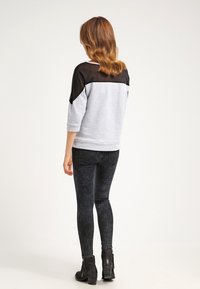 Grijze sweat met zwart mesh bovenpaneel, driekwarts mouwen, gecombineerd met donkere skinny jeans en zwarte enkellaarsjes.