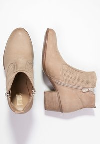 Vaa'at polvi beigessä värissä, valmistettu sileästä nahasta ja teksturoiduista yksityiskohdista. Niissä on sivuvetoketju, pyöreä varvas ja vaatimaton lohko korko.