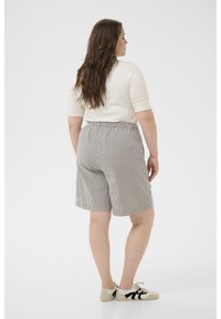 Shorts rayés avec une taille élastique, longueur mi-cuisse, associés à un haut ajusté de couleur claire et des baskets décontractées.
