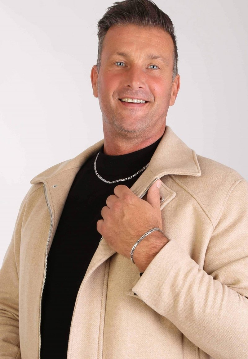 Beige wollen jas met een rits, zwarte coltrui eronder, zilveren ketting en armband, gladde texturen en casual pasvorm.