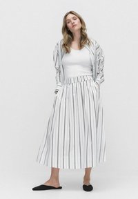 Jupe longue à rayures blanches avec une taille élastique, associée à un débardeur blanc ajusté et une veste à rayures oversize assortie. Chaussures slip-on noires.