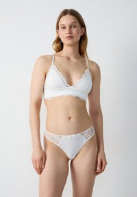 Brassière en dentelle blanche avec des bords en forme de coquille et des bretelles réglables, associée à une culotte assortie avec des accents en dentelle et un petit nœud décoratif.
