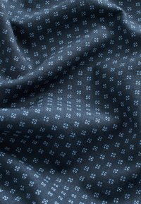 Tissu bleu foncé avec un petit motif floral composé de quatre points bleu clair, présenté en plis doux.