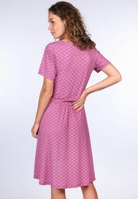 Kurzes, knielanges Kleid aus pinkem Stoff mit einem wiederholenden Blattform. Es hat eine geraffte Taille und eine lockere Passform.