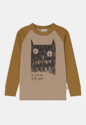 Camiseta raglán de manga larga para niño con mangas marrones y cuerpo beige, con un dibujo en negro de una cabeza de monstruo y el texto "Un amigo de la noche."