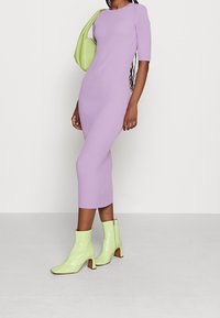 Robe midi côtelée en violet pastel avec un col rond et des manches courtes, associée à des bottines vernies vert citron et un sac assorti.