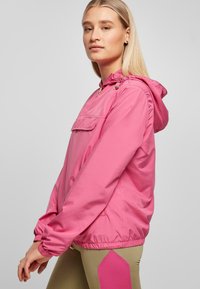 Roze lichtgewicht jack met een capuchon, voork pocket, elastische manchetten en een aangesnoerd tailleband. Vlotte textuur; minimalistische hardwaredetails.