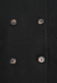 Manteau en laine noire avec quatre grands boutons gris foncé disposés en deux paires verticales sur le panneau avant.