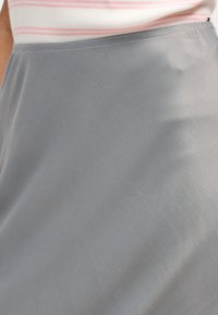 Κοντινό πλάνο ενός ατόμου που φοράει λευκό και ροζ ριγέ πουκάμισο, βαλμένο σε μια γκρι φούστα με ψηλή μέση.