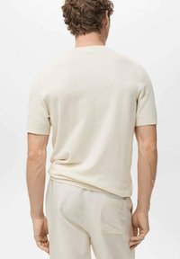 Light beige short-sleeve sweater with a textured knit, crew neck, and a relaxed fit, worn with light-colored pants.