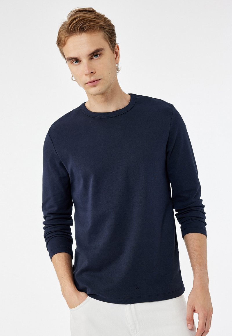 Camiseta de algodón azul marino de manga larga con cuello redondo y puños acanalados, con un corte relajado y un sutil detalle del logo en el dobladillo.