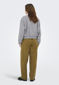 Sweat-shirt gris en maille avec un ourlet côtelé, associé à un pantalon ample taille haute de couleur vert olive. Des chaussures noires épaisses complètent la tenue.