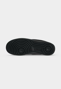 Μαύρη σόλα αθλητικού παπουτσιού Nike, εμφανιζόμενη από κάτω, με κυκλικά σχέδια πέλματος και το λογότυπο της Nike στη μέση της σόλας.