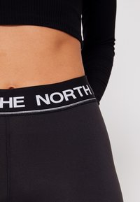 Mustat legginsit, joissa on leveä vyötärönauha, johon on painettu valkoisella "THE NORTH". Kangas on sileä, hieman kiiltävä ja ompelut ovat minimissään.