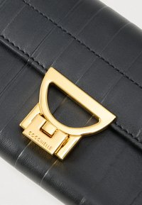Black leather wallet with textured stripes and gold clasp engraved with "COCCINELLE" brand name.