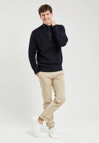 Granatowy sweter dzianinowy z półzapinem, w połączeniu z beżowymi chinosami i białymi trampkami. Gładka tekstura, dopasowany krój i casualowy styl.