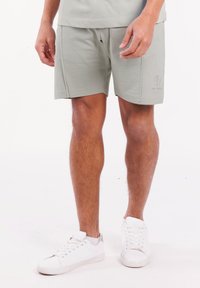 Lichtgroene shorts gemaakt van zachte stof, met een relaxte pasvorm, zijzakken en een subtiel logo op de zoom. G gedragen met witte sneakers.