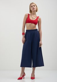 Haut court tricoté rouge avec des culottes larges marine. Le modèle porte des talons hauts rouges et un bracelet. Design simple, texture lisse et couleurs vives.