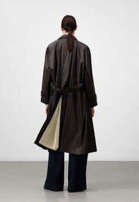 Lang, donker trenchcoat met een riem, met een lichtgekleurde voering en een gesplitste achterkant. Gemaakt van glanzende, gladde stof.