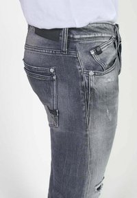 Grijze denim jeans met een slim fit, versleten details, meerdere zakken en een gladde textuur. Iconische merkbranding op de tailleband.