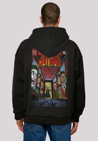 Felpa nera con cappuccio che presenta una grafica colorata in stile fumetto sul retro, raffigurante Batman e vari personaggi in pannelli incorniciati.